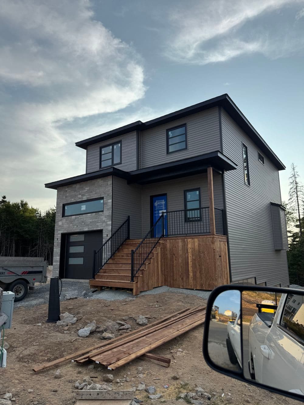 Modern two-story home with a blue door, wooden steps, and stone accents, under a clear sky.