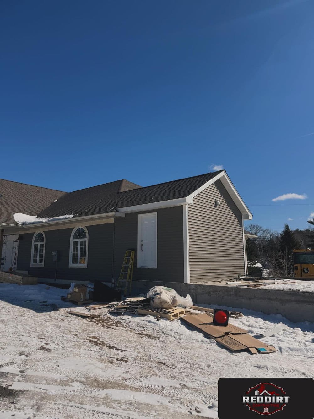 New home construction with snow, blue sky, and building materials visible in the foreground.