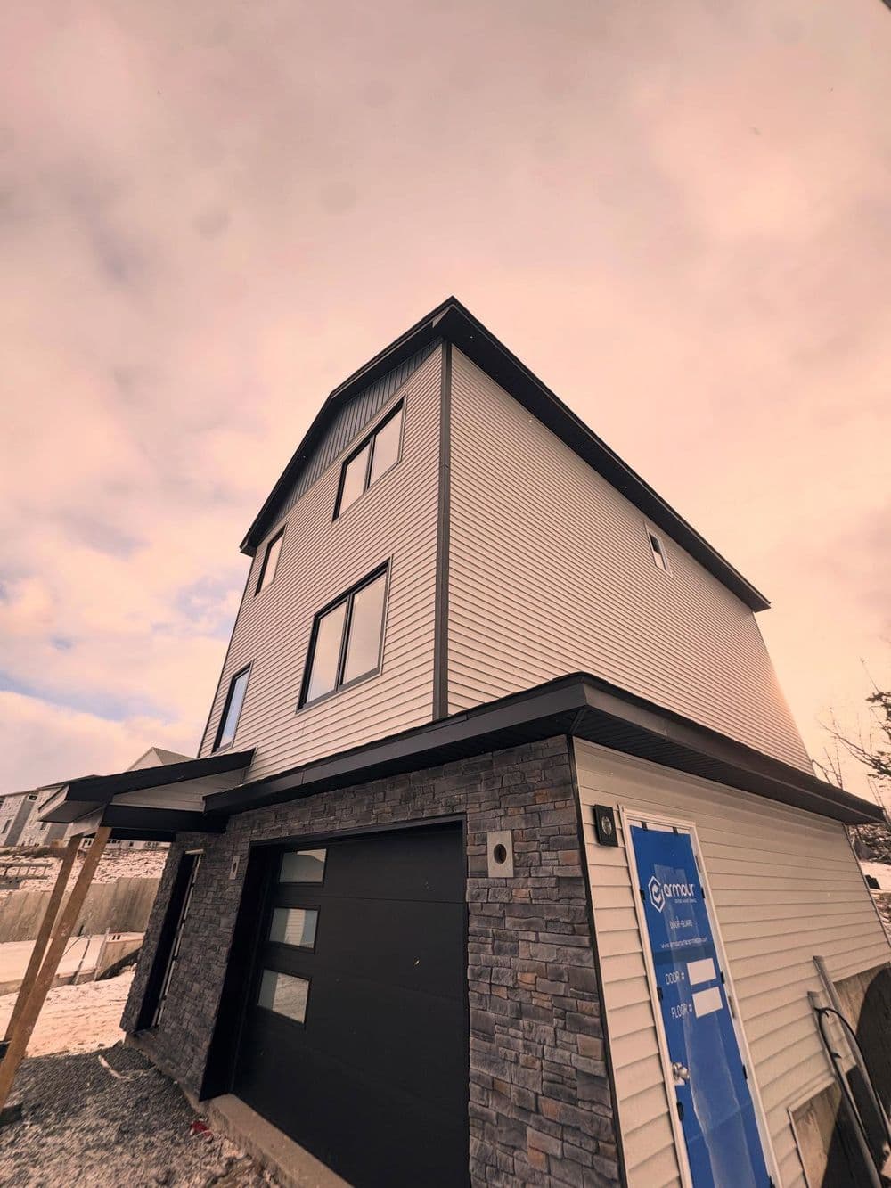 Modern three-story house with stone accents and a black garage door under a cloudy sky.