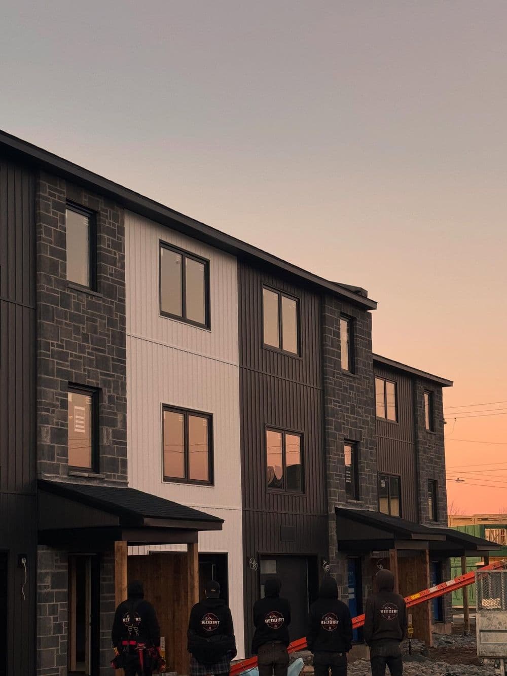 New modern homes with black and white exteriors at sunset, construction workers in foreground.