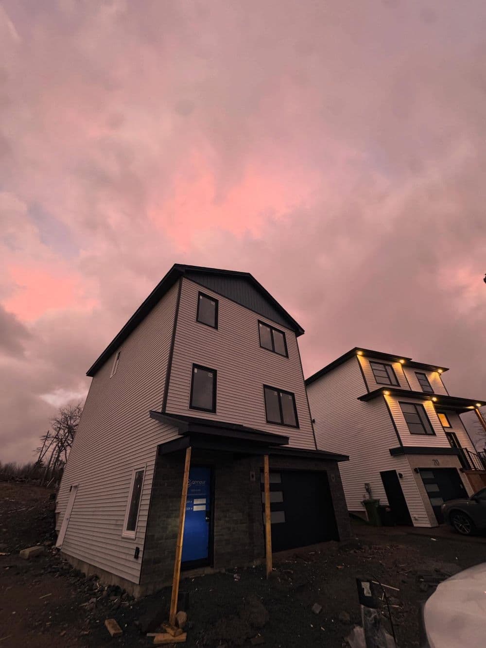 Modern two-story house with blue door, set against a pink sky at sunset.
