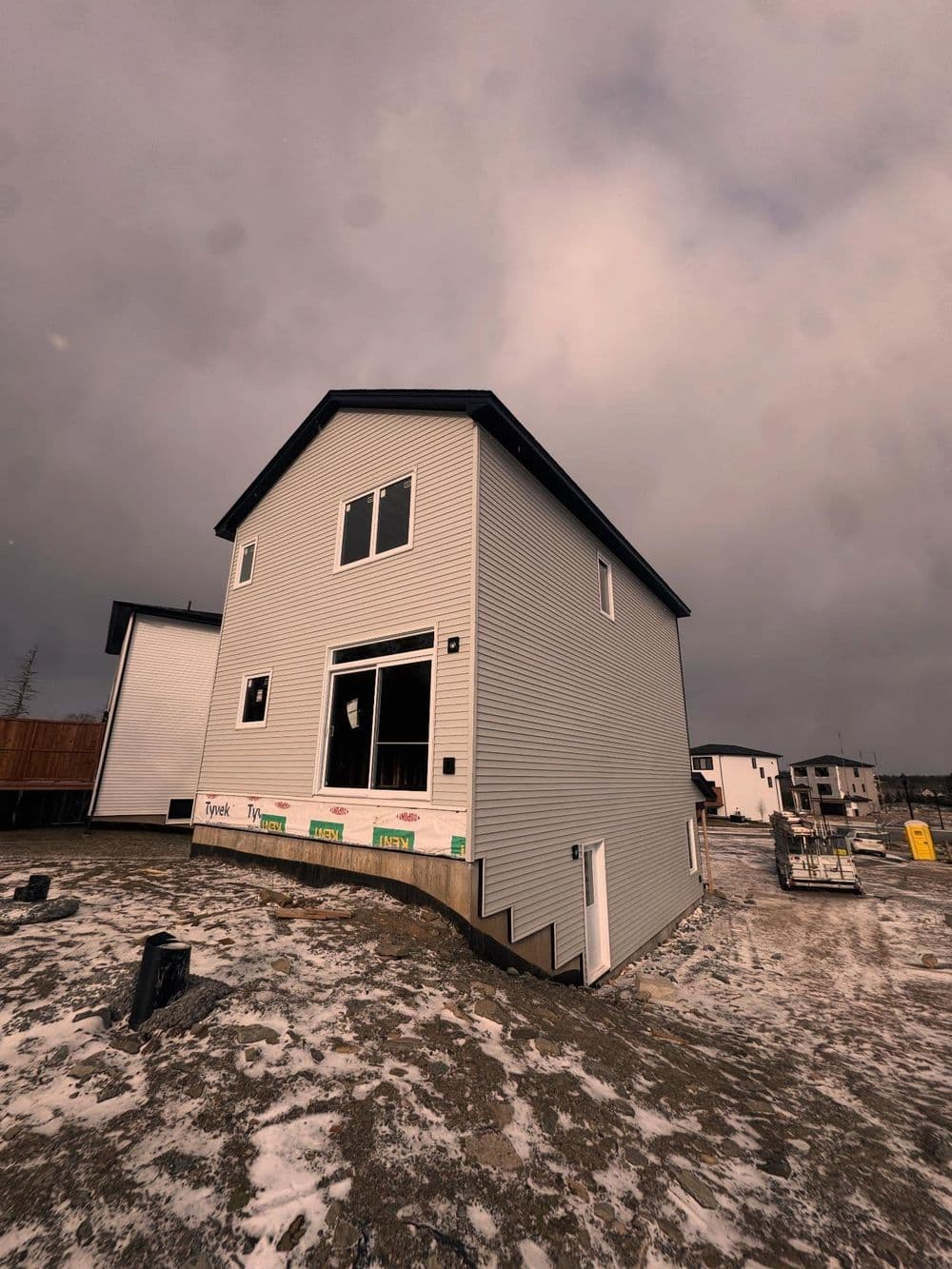Modern two-story house under construction with gray siding and cloudy sky background.