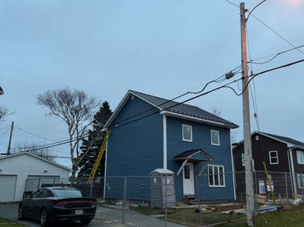 Blue house under construction with a ladder, surrounded by a fence and utility poles.