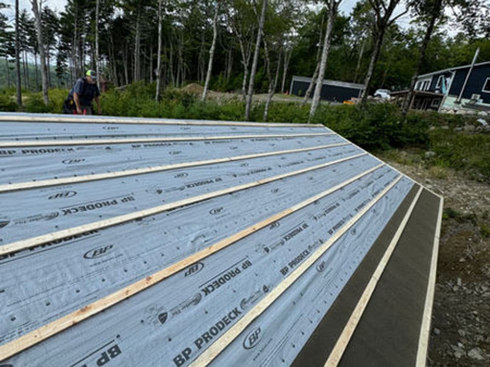 Roof installation in progress with insulated panels and wooden beams amid a forested area.