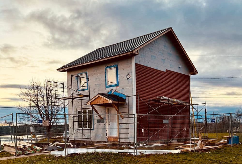 Newly constructed house under renovation, surrounded by a construction fence at sunset.