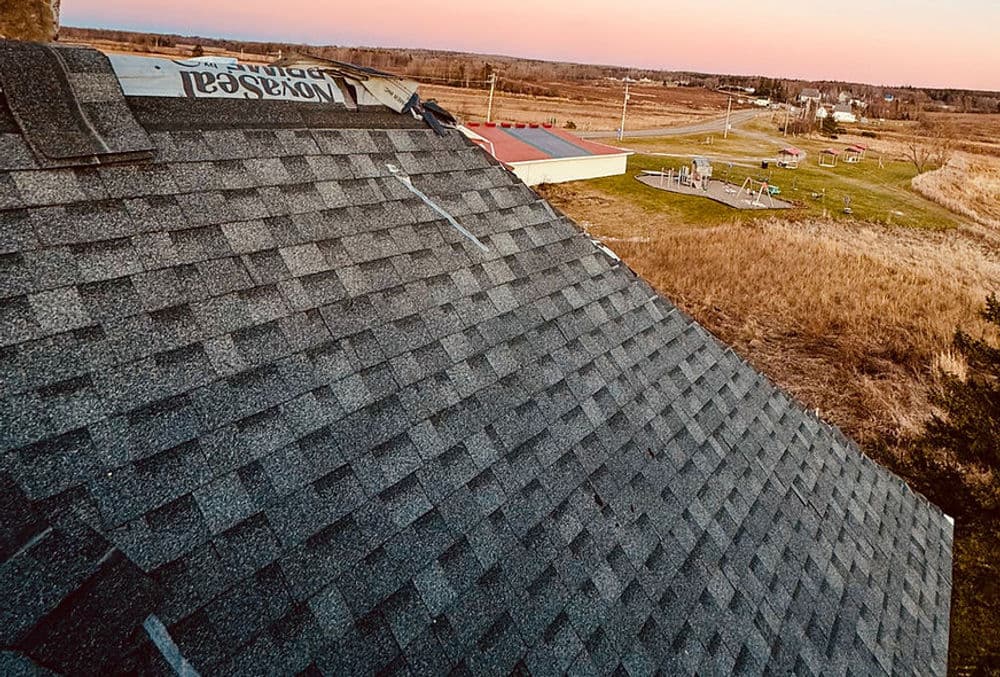 Asphalt shingle roof with nearby open field and playground at sunset.