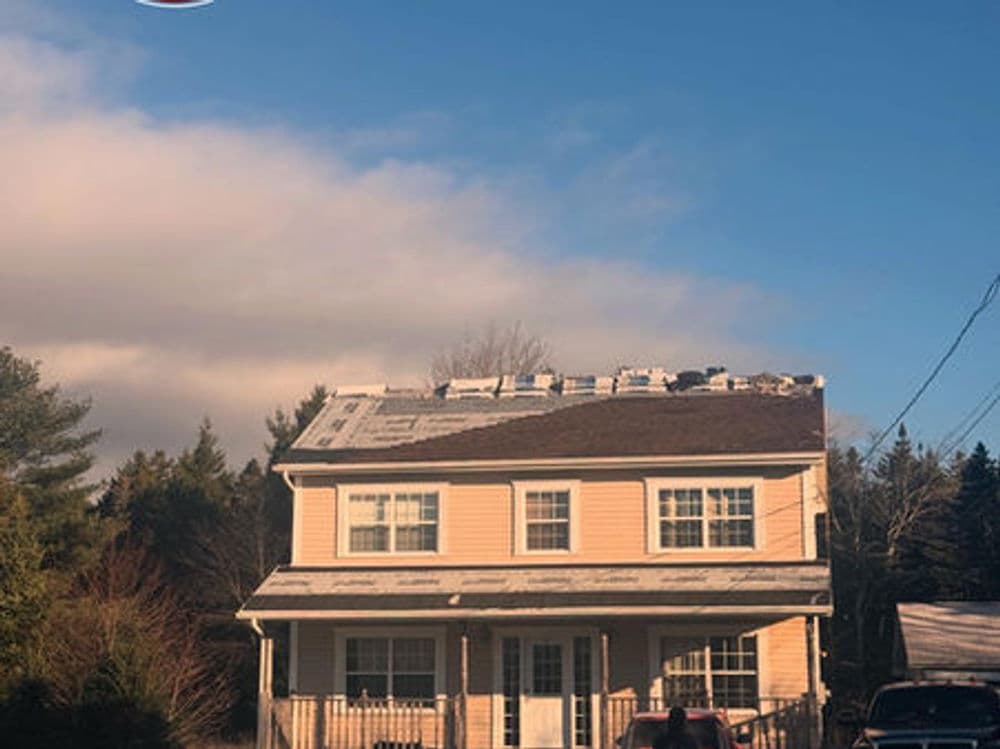 Two-story house with a roof under construction and clear blue sky in the background.